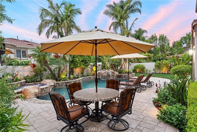 patio terrace at dusk featuring a fenced in pool, fence, and outdoor dining space
