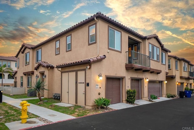 multi unit property with a garage, a balcony, a tiled roof, and stucco siding