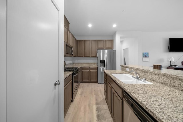 kitchen featuring light wood finished floors, light stone countertops, a sink, recessed lighting, and appliances with stainless steel finishes