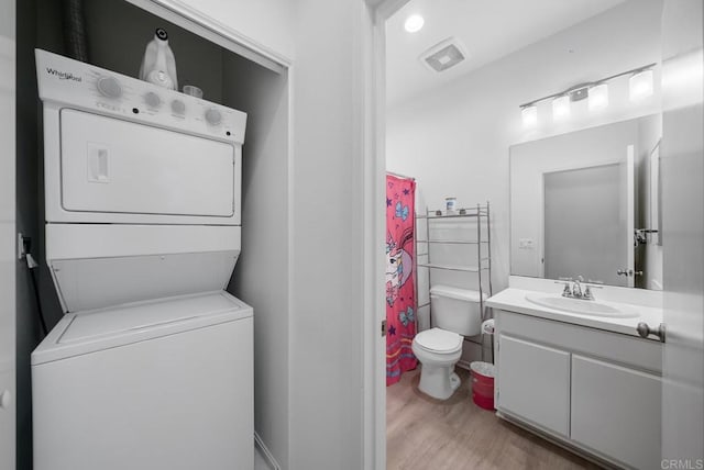 full bathroom with toilet, wood finished floors, stacked washing maching and dryer, and vanity