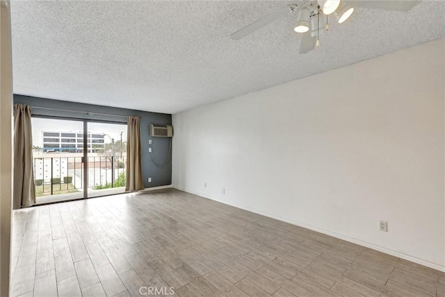 spare room with a wall mounted air conditioner, a ceiling fan, baseboards, a textured ceiling, and wood finished floors