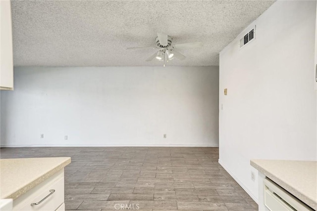 unfurnished dining area with light wood-style flooring, ceiling fan, baseboards, visible vents, and a textured ceiling