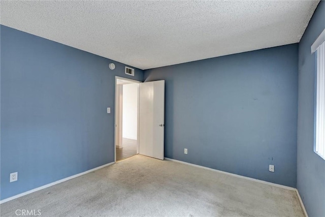unfurnished room with a textured ceiling, visible vents, carpet, and baseboards