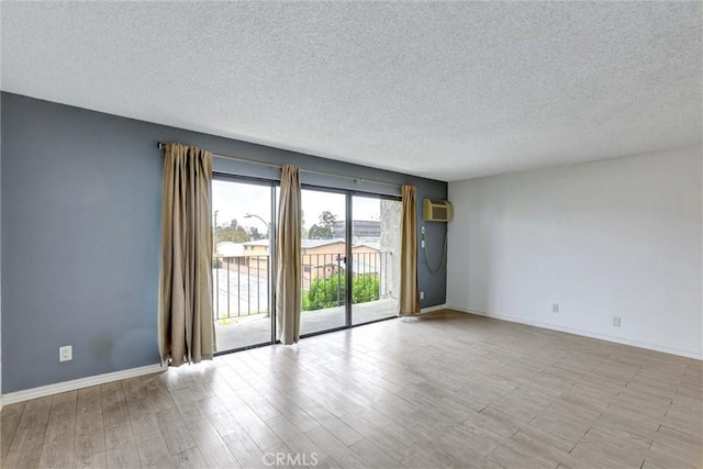 spare room with a textured ceiling, a wall mounted AC, wood finished floors, and baseboards