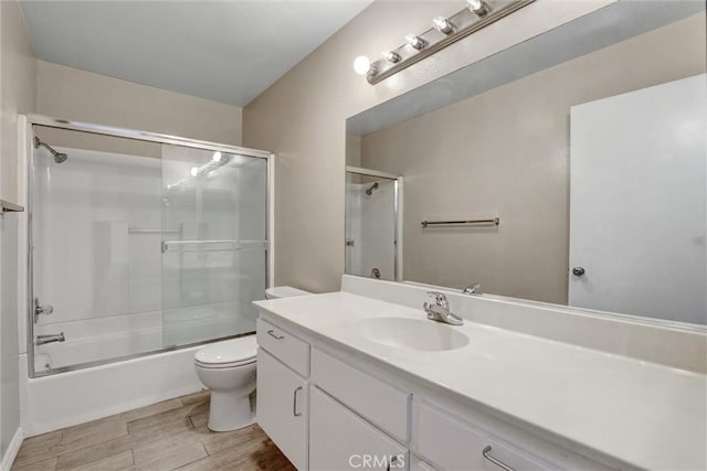 bathroom featuring toilet, vanity, combined bath / shower with glass door, and wood finished floors
