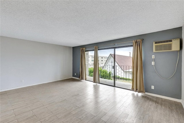 unfurnished room featuring baseboards, wood finished floors, a textured ceiling, and a wall mounted AC