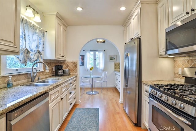 1956 E Woodlyn Rd, Pasadena, CA 91104 - kitchen featuring appliances with stainless steel finishes, a sink, arched walkways, light wood-type flooring, and backsplash