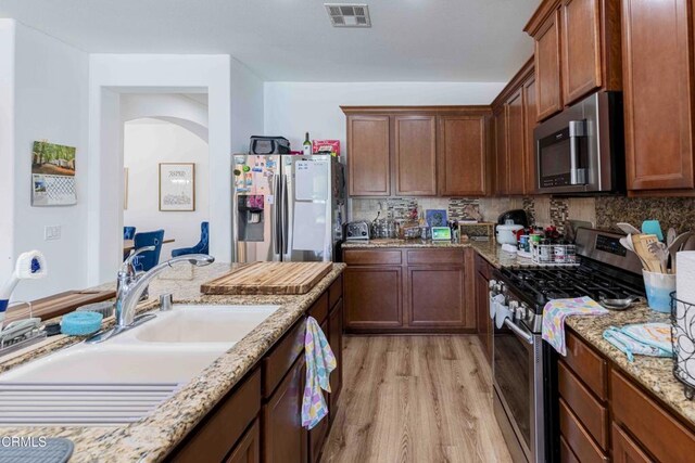 10909 Rainwater Ln, Bakersfield, CA 93306 - kitchen featuring stainless steel appliances, light wood-type flooring, decorative backsplash, and light stone countertops