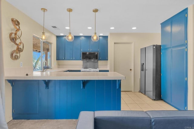 kitchen with stainless steel appliances, blue cabinets, tile counters, a peninsula, and a sink