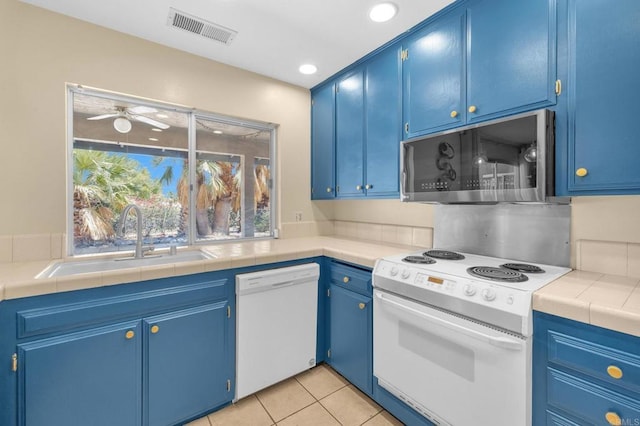 kitchen featuring white appliances, a sink, blue cabinets, light tile patterned floors, and ceiling fan