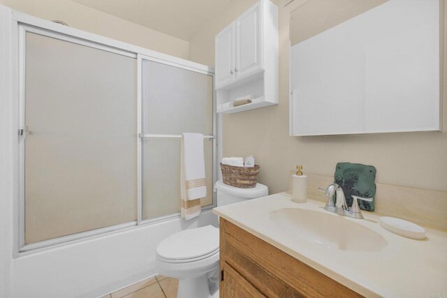 bathroom featuring toilet, vanity, tile patterned floors, and enclosed tub / shower combo