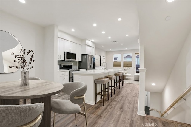 kitchen featuring stainless steel appliances, a sink, a center island with sink, light wood-type flooring, and recessed lighting