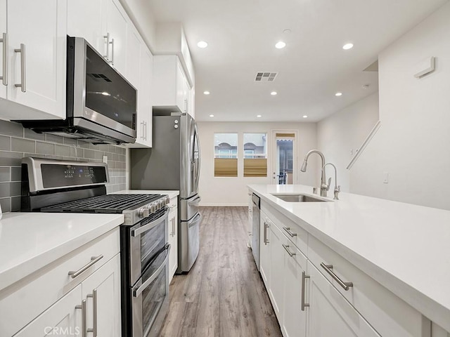 15331 Jasmine Ln Unit 105, Gardena, CA 90249 - kitchen with stainless steel appliances, a sink, light wood finished floors, backsplash, and white cabinetry