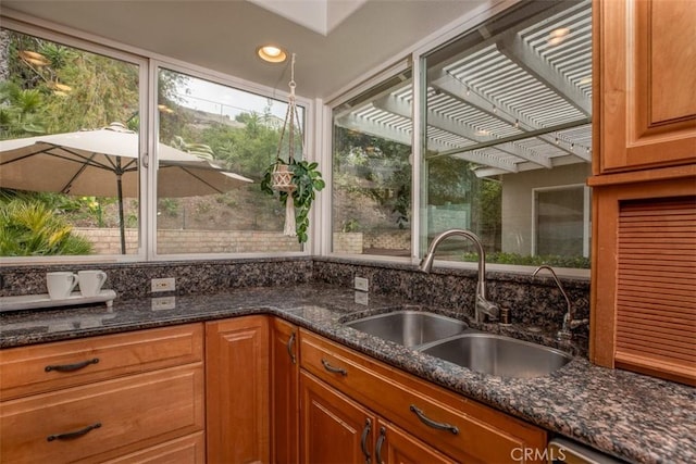 kitchen featuring dark stone countertops, recessed lighting, a sink, and brown cabinetry