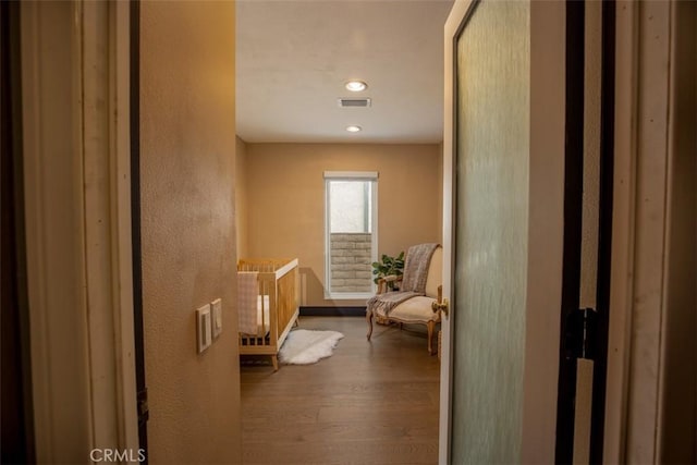hall with visible vents, a textured wall, wood finished floors, and baseboards