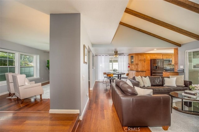 living area with baseboards, wood finished floors, ceiling fan, and lofted ceiling with beams