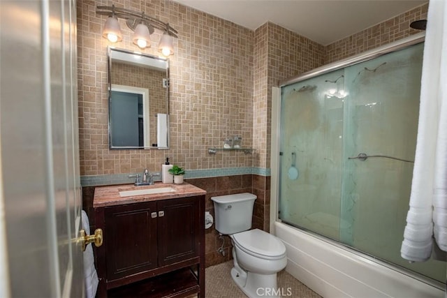 full bath featuring tile patterned floors, tile walls, enclosed tub / shower combo, toilet, and vanity