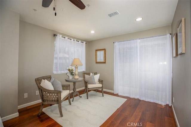 sitting room with wood finished floors, visible vents, a ceiling fan, and baseboards