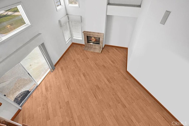 unfurnished living room with wood finished floors, baseboards, and a brick fireplace