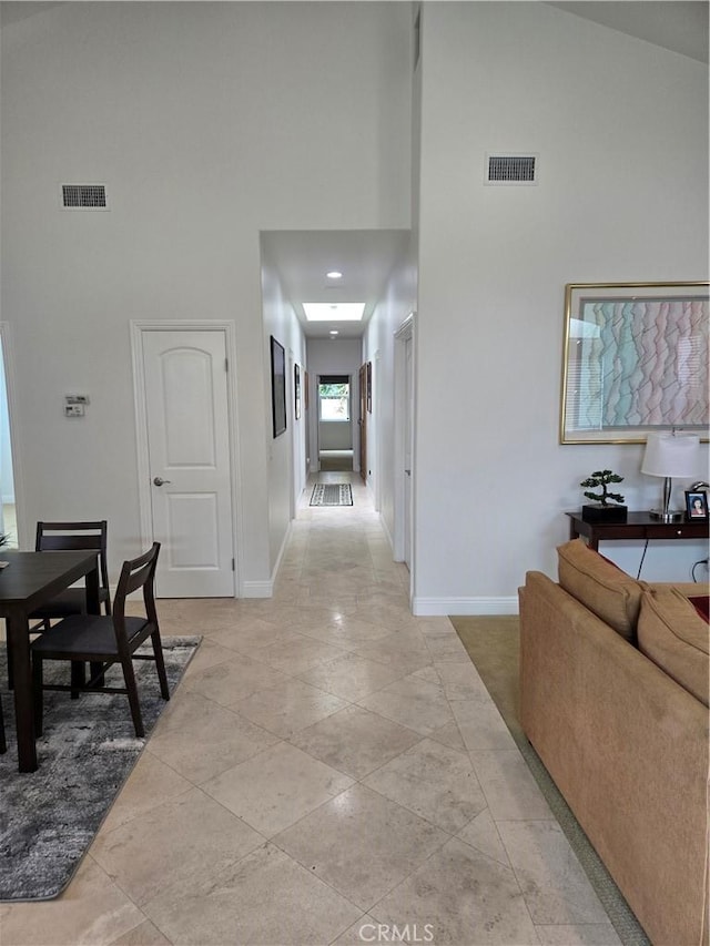 hallway with a high ceiling, visible vents, and baseboards