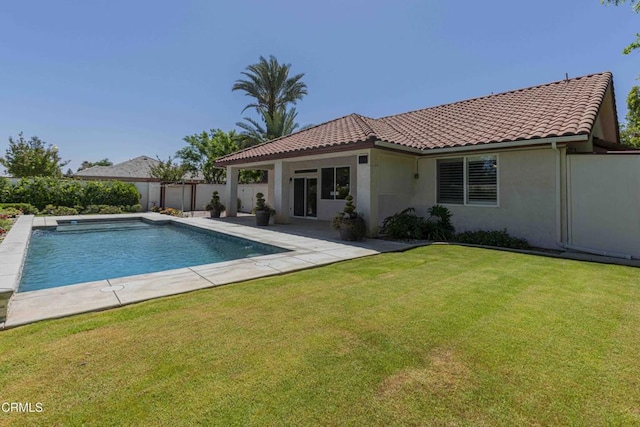rear view of house featuring fence, stucco siding, a tiled roof, and a lawn