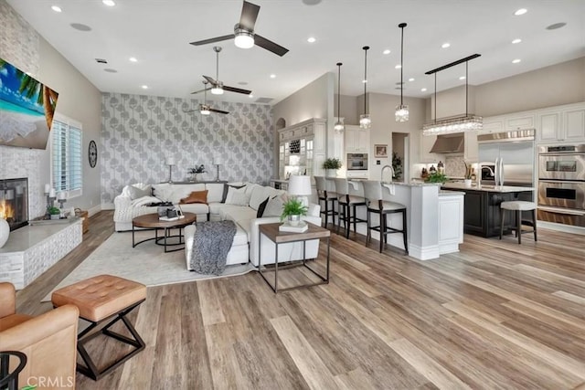 living area with ceiling fan, wallpapered walls, light wood finished floors, an accent wall, and recessed lighting