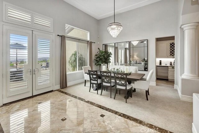 dining space featuring decorative columns, french doors, a towering ceiling, baseboards, and an inviting chandelier