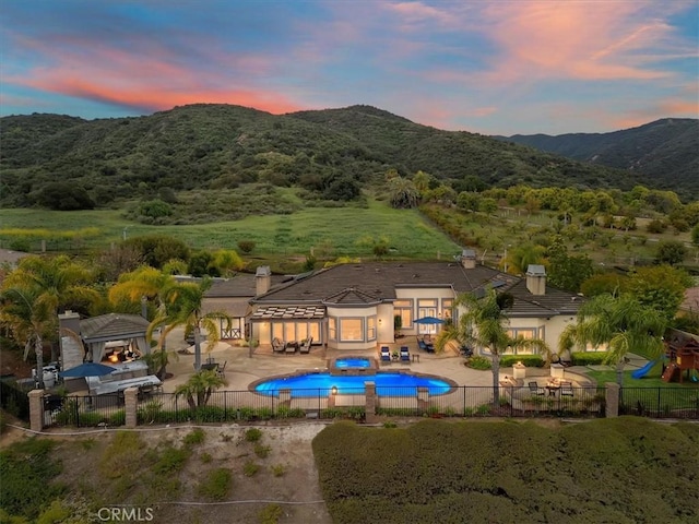 pool at dusk featuring a fenced in pool, a mountain view, a fenced backyard, and a patio area
