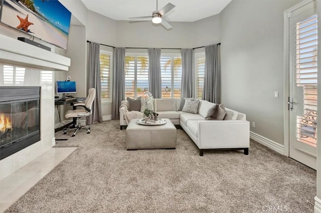 carpeted living area with baseboards, ceiling fan, a tiled fireplace, and a healthy amount of sunlight
