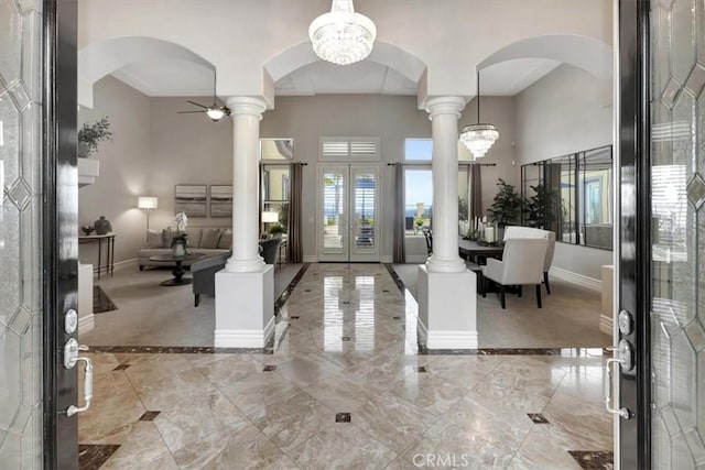 foyer entrance featuring baseboards, arched walkways, marble finish floor, and ornate columns