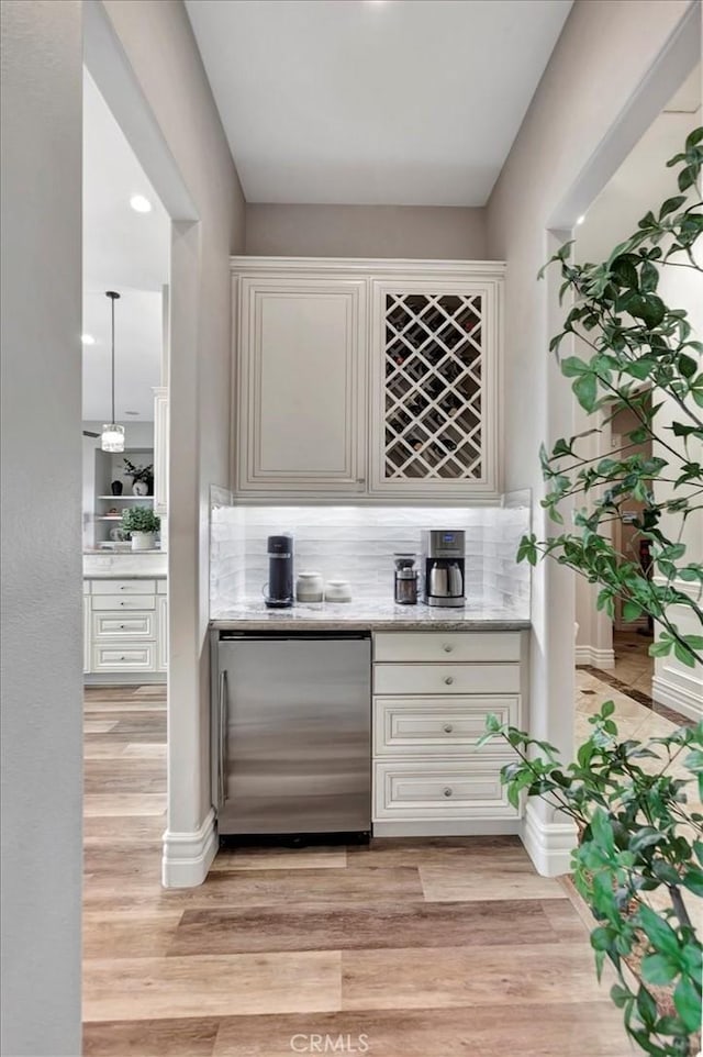 bar featuring stainless steel fridge, a bar, backsplash, and light wood-style flooring