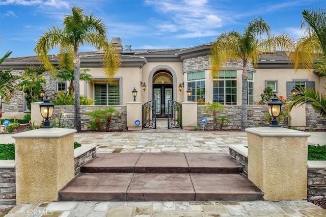 mediterranean / spanish home with a tile roof, stucco siding, roof mounted solar panels, a gate, and french doors
