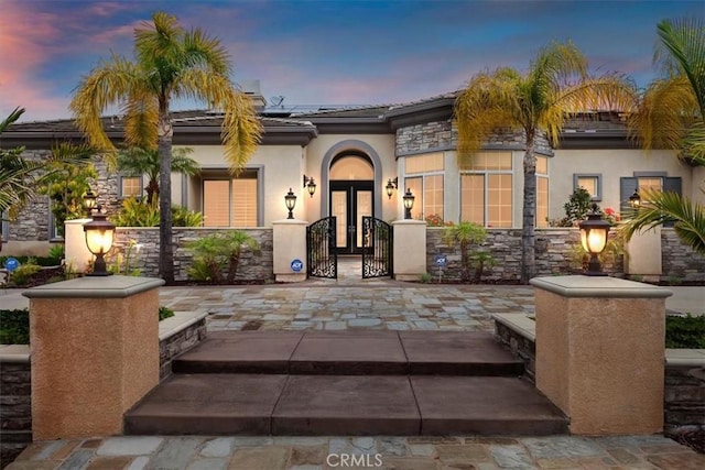 view of front of house featuring french doors, a tile roof, solar panels, a gate, and stucco siding
