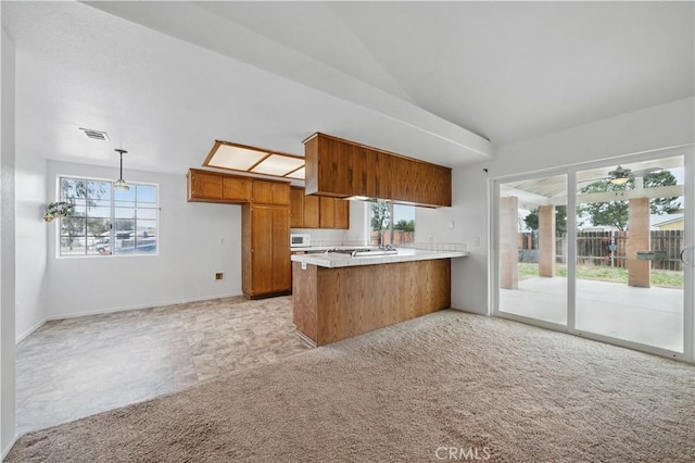 kitchen with a peninsula, lofted ceiling, brown cabinets, visible vents, and light countertops