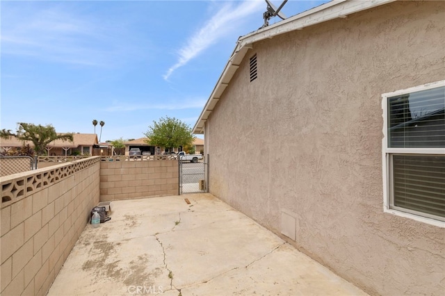 view of side of home with a patio area, fence, stucco siding, and a gate