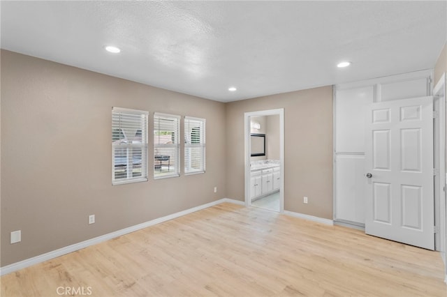 unfurnished bedroom featuring ensuite bath, recessed lighting, light wood-style flooring, and baseboards