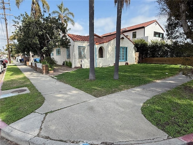 mediterranean / spanish-style home with a front yard, stucco siding, a tiled roof, and fence