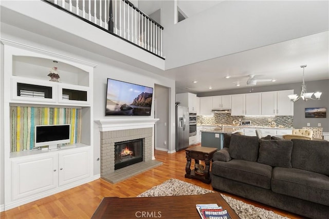living room with a brick fireplace, light wood finished floors, a chandelier, and baseboards