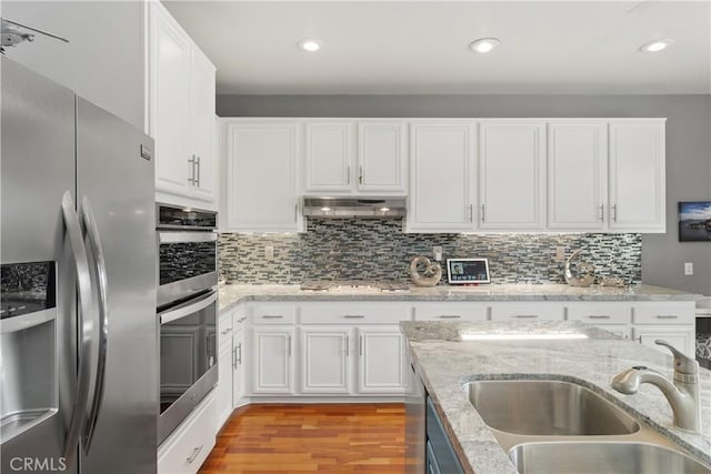 kitchen featuring white cabinets, a sink, light wood-style floors, stainless steel appliances, and under cabinet range hood