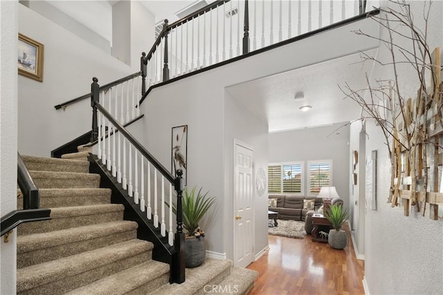 staircase with baseboards, wood finished floors, and a high ceiling