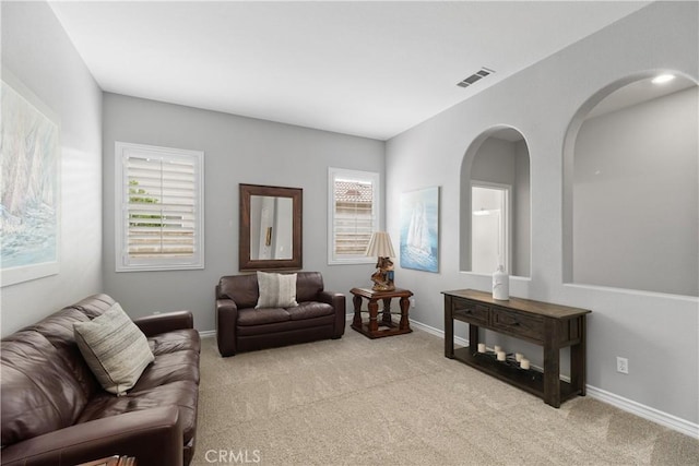 living area with baseboards, visible vents, arched walkways, and light colored carpet