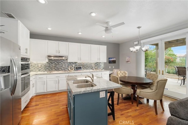 kitchen with a sink, under cabinet range hood, tasteful backsplash, white cabinetry, and appliances with stainless steel finishes