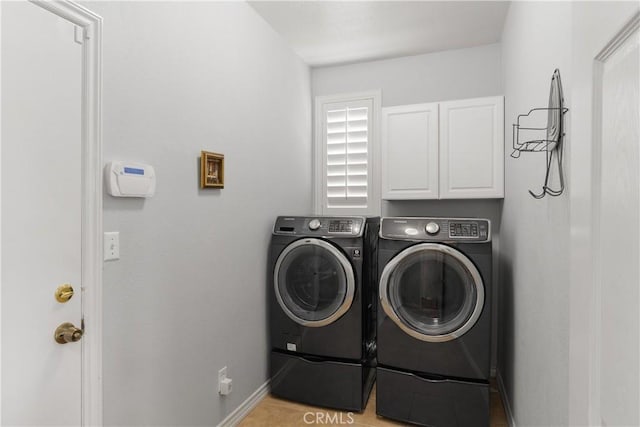 clothes washing area featuring baseboards, cabinet space, and washing machine and dryer