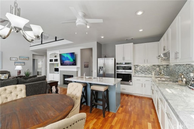 kitchen with stainless steel appliances, white cabinets, a kitchen bar, a ceiling fan, and open floor plan
