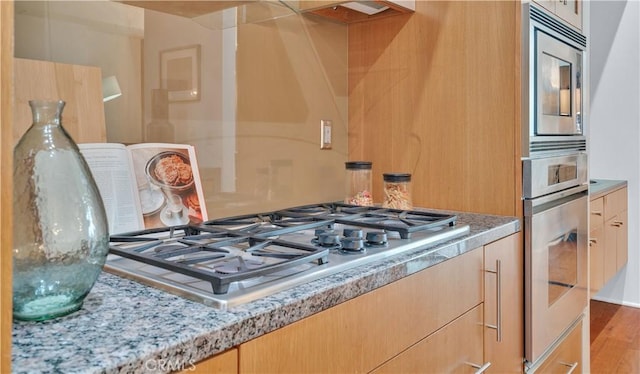 details with appliances with stainless steel finishes, light stone counters, and light brown cabinetry