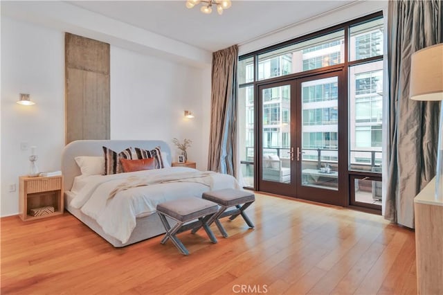 bedroom featuring access to exterior, an inviting chandelier, light wood-style floors, and french doors