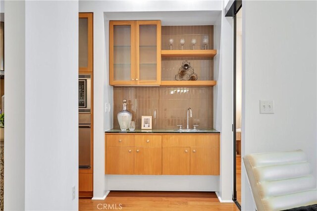 bar with stainless steel microwave, indoor wet bar, a sink, decorative backsplash, and light wood-style floors