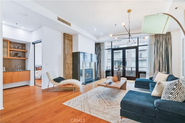 living room featuring visible vents, light wood-style floors, a lit fireplace, recessed lighting, and french doors