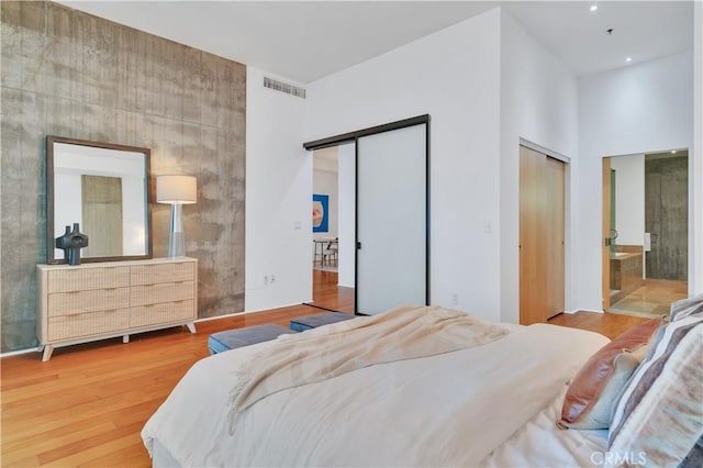bedroom with recessed lighting, wood finished floors, two closets, visible vents, and a towering ceiling