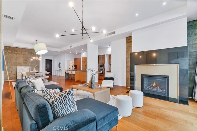 living area featuring wood finished floors, visible vents, a tray ceiling, and a chandelier